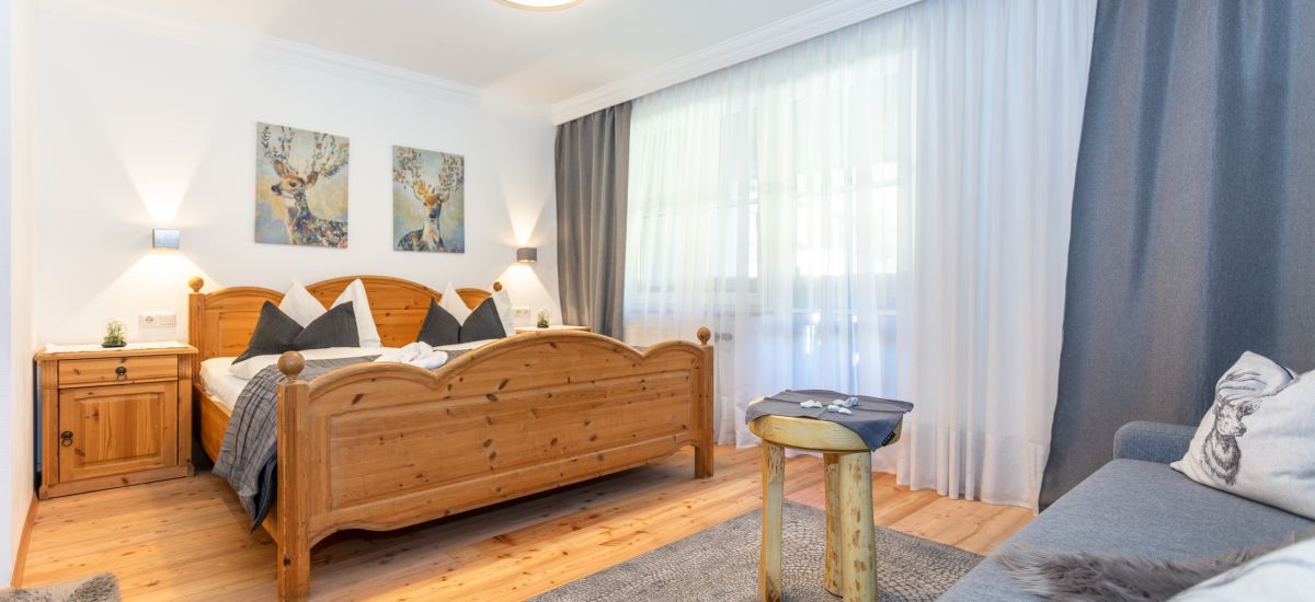 Zirbenholzbett mit Nachtkästchen, Kasten und Sommerblumenstrauß im Hotel Gasthof Camping Andrelwirt in Rauris im Salzburgerland.